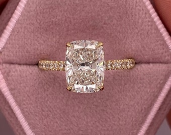 Op de afbeelding: Een vierkante diamanten verlovingsring met een gouden band en een halo van kleinere diamanten. De ring zit in een roze fluwelen ringdoos.