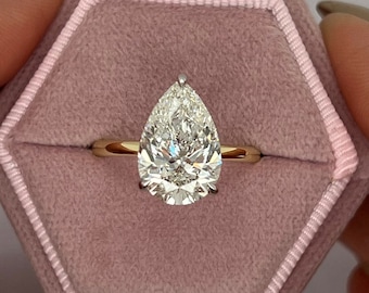May include: A pear-shaped diamond engagement ring set in a gold band, displayed in a pink velvet ring box.