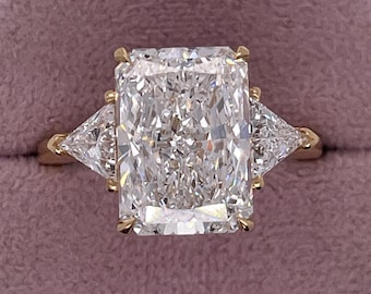 May include: A gold ring featuring a large, rectangular, clear diamond in the centre and two smaller, triangular, clear diamonds on either side.