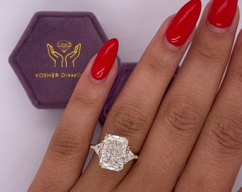 May include: A gold ring featuring a large, rectangular, clear diamond in the centre and two smaller, triangular, clear diamonds on either side. The ring is worn on a person's finger.