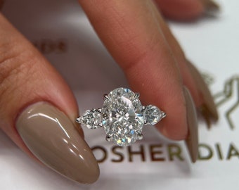 May include: A silver ring with a large oval-shaped diamond in the center and two smaller pear-shaped diamonds on either side.