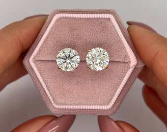 May include: A pair of round diamond earrings in a pink velvet box. The earrings are set in gold.