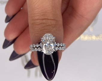 Könnte beinhalten: Nahaufnahme eines silbernen Verlobungsringes mit einem großen ovalen Diamanten. Der Ring hat ein doppeltes Band mit kleinen Diamanten, die in das Band eingefasst sind.