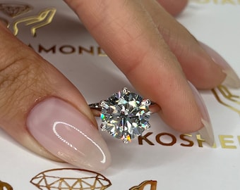 May include: A close-up of a silver ring with a large, round, clear diamond. The ring is on a finger with light pink nail polish.