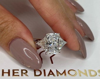 May include: A  diamond engagement ring with a large, rectangular-shaped center stone and two smaller, triangular-shaped stones on either side. The ring is set in white gold.