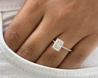 May include: A rose gold engagement ring with a large, rectangular, clear diamond center stone and a band of smaller diamonds.