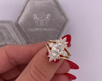 May include: A gold engagement ring with a large oval-shaped center diamond surrounded by smaller diamonds in a floral design. The ring is on a finger with red nail polish.
