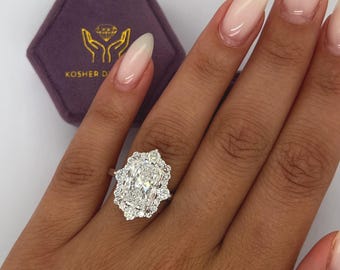May include: A large oval-shaped diamond engagement ring with a halo of smaller diamonds. The ring is set in white gold and is worn on a hand with light pink nail polish.