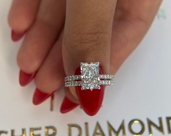 May include: A radiant-cut diamond engagement ring with a pave band, paired with a matching diamond band. The rings are set on a white surface with gold lettering that reads "FISHER DIAMONDS". The image is a close-up shot.