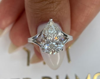 Puede incluir: Un anillo de compromiso de diamante de forma pera con una montura de doble garra. El anillo está engastado en oro blanco y presenta un gran diamante brillante.