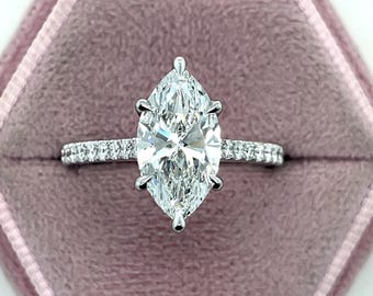 Op de afbeelding: Een verlovingsring met een marquise-geslepen diamant met een pavé-diamanten band gezet in een witgouden setting. De ring zit in een roze fluwelen ringdoos.