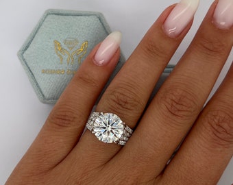 Könnte beinhalten: Nahaufnahme einer Hand, die einen silbernen Ring mit einem großen, runden, klaren Diamanten in der Mitte und kleineren Diamanten trägt, die den Mitteldiamanten umgeben. Der Ring ist auf einem silbernen Band mit einer doppelten Reihe kleinerer Diamanten gefasst.