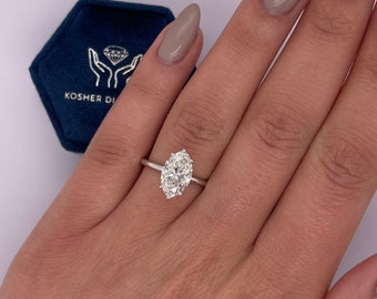 May include: A silver ring with an oval-shaped diamond set in a prong setting. The ring is on a person's finger.