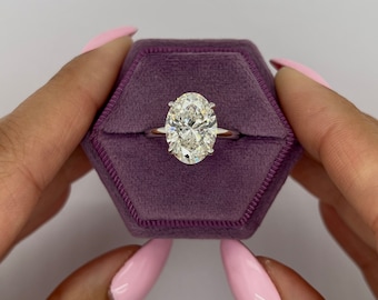 Op de afbeelding: Een grote, ovale diamanten verlovingsring gezet in een witgouden band. De ring wordt gepresenteerd in een paarse fluwelen ringdoos.