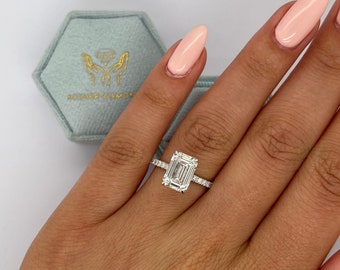 May include: A silver ring with an emerald cut diamond and a pave diamond band. The ring is on a finger with light pink nail polish.