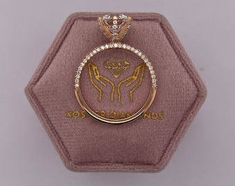 May include: A gold engagement ring featuring a large round diamond centre stone, surrounded by smaller diamonds in a halo setting. The ring is displayed in a velvet ring box with the inscription "Koster Diamonds".