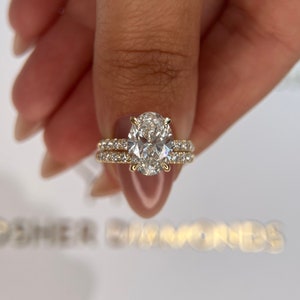 May include: A gold engagement ring with an oval-shaped diamond center stone and a diamond band. The ring is set on a white background.
