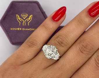 May include: A three-stone diamond engagement ring with a large oval center stone and two smaller oval side stones. The ring is set in a white gold band.
