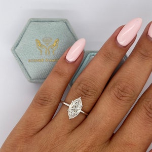 May include: A close-up of a hand wearing a silver ring with a large, clear marquise-shaped diamond. The ring is set in a simple band.