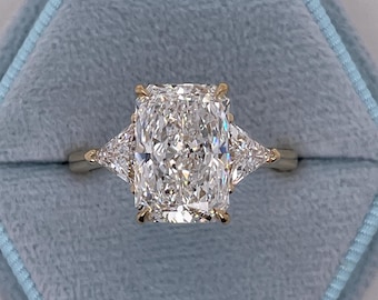 May include: A gold ring featuring a large, cushion-cut diamond with two smaller, triangular diamonds on either side.
