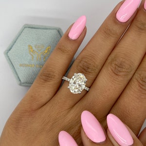 Op de afbeelding: Een zilveren ring met een grote ovale diamant gezet in een pavé setting. De ring wordt gedragen op een hand met roze nagellak.