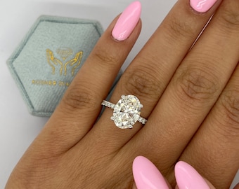 Puede incluir: Un anillo de plata con un gran diamante de forma ovalada engastado en pavé. El anillo está en una mano con esmalte de uñas rosa.