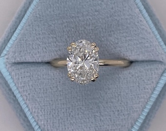 May include: A gold ring with a large oval-shaped diamond set in a prong setting. The ring is in a blue velvet ring box.