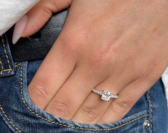 May include: A silver ring with a large, clear, cushion-cut diamond set in a pave band.