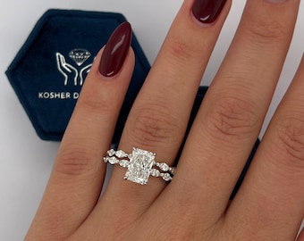 May include: A close-up of a hand wearing a silver ring with a large rectangular diamond and a smaller diamond band. The ring is on the third finger of the left hand. The hand is wearing dark red nail polish.