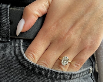 Könnte beinhalten: Ein goldener Ring mit einem großen ovalen Diamanten, der in der Mitte sitzt. Der Ring befindet sich an einem Finger einer Person, und die Hand der Person befindet sich in einer Tasche.