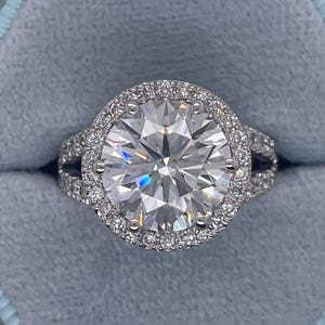 Op de afbeelding: Een grote, ronde, heldere diamanten verlovingsring met een dubbele halo-setting. De ring is gezet in witgoud en heeft een grote middelste steen die omgeven is door twee rijen kleinere diamanten.