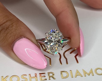 Puede incluir: Primer plano de un anillo de plata con un gran diamante de forma ovalada. El anillo está en un dedo con esmalte de uñas rosa.