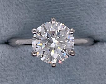 May include: A round, clear diamond engagement ring set in a silver band. The diamond is large and has many facets.