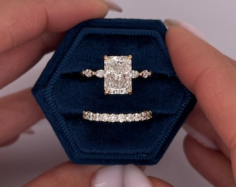 May include: A pair of diamond rings in a blue velvet ring box. The engagement ring features a large, rectangular-shaped diamond with smaller diamonds on the band. The wedding band is a thin band with small diamonds set in a pave setting.
