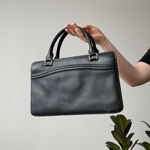 May include: A black leather handbag with two top handles and a gold clasp.