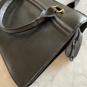 May include: A black leather tote bag with gold hardware and a zipper closure.