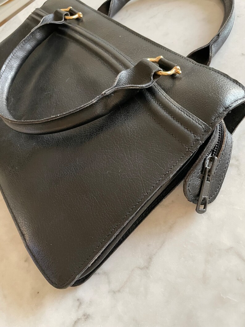 May include: A black leather tote bag with gold hardware and a zipper closure.