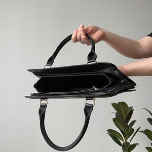May include: A black leather tote bag with gold hardware and two top handles. The bag is open and empty.