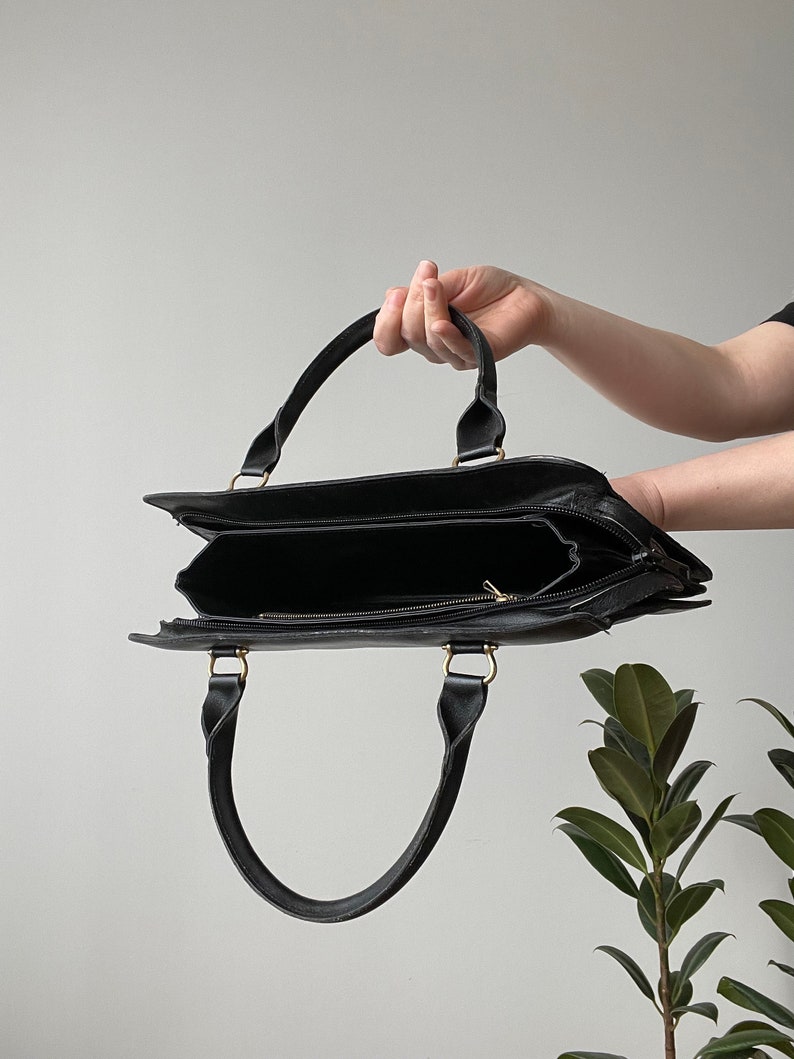 May include: A black leather tote bag with gold hardware and two top handles. The bag is open and empty.