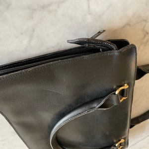 May include: A black leather satchel with a gold buckle and a zipper closure. The bag has a top handle and a shoulder strap.