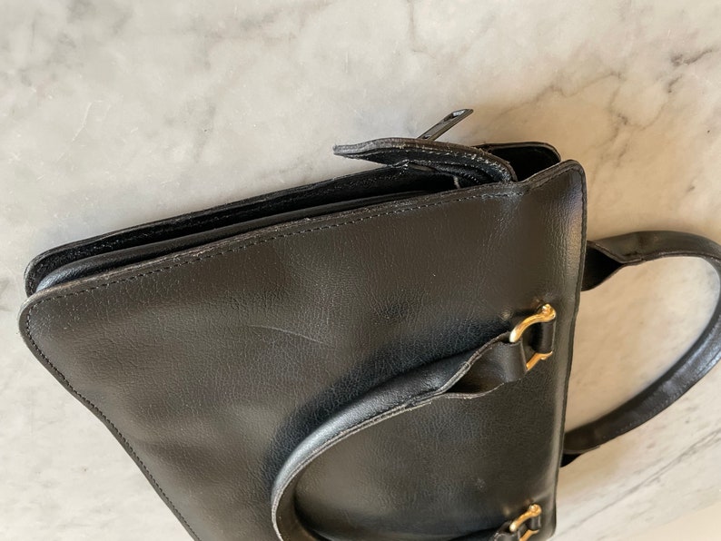 May include: A black leather satchel with a gold buckle and a zipper closure. The bag has a top handle and a shoulder strap.