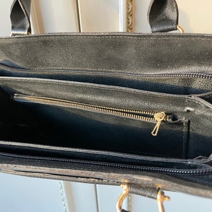 May include: Black leather handbag with two zippered compartments and a gold zipper pull.