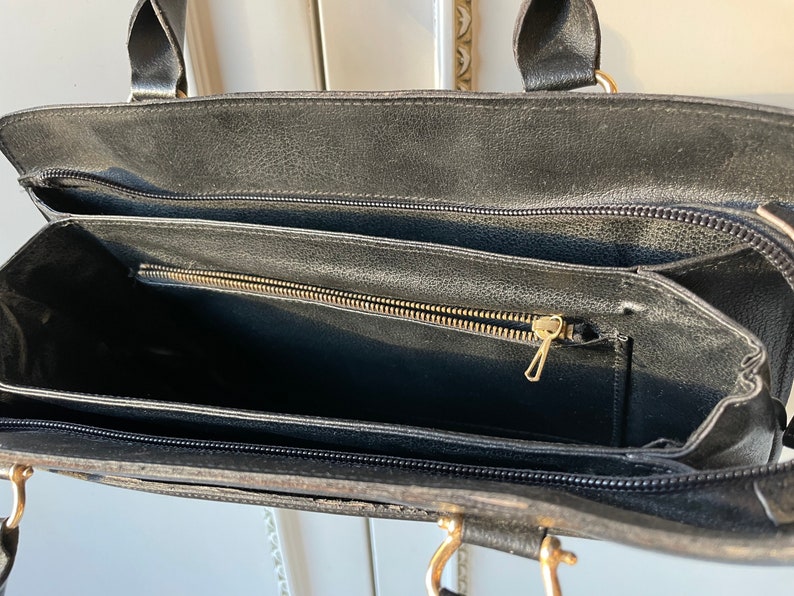 May include: Black leather handbag with two zippered compartments and a gold zipper pull.