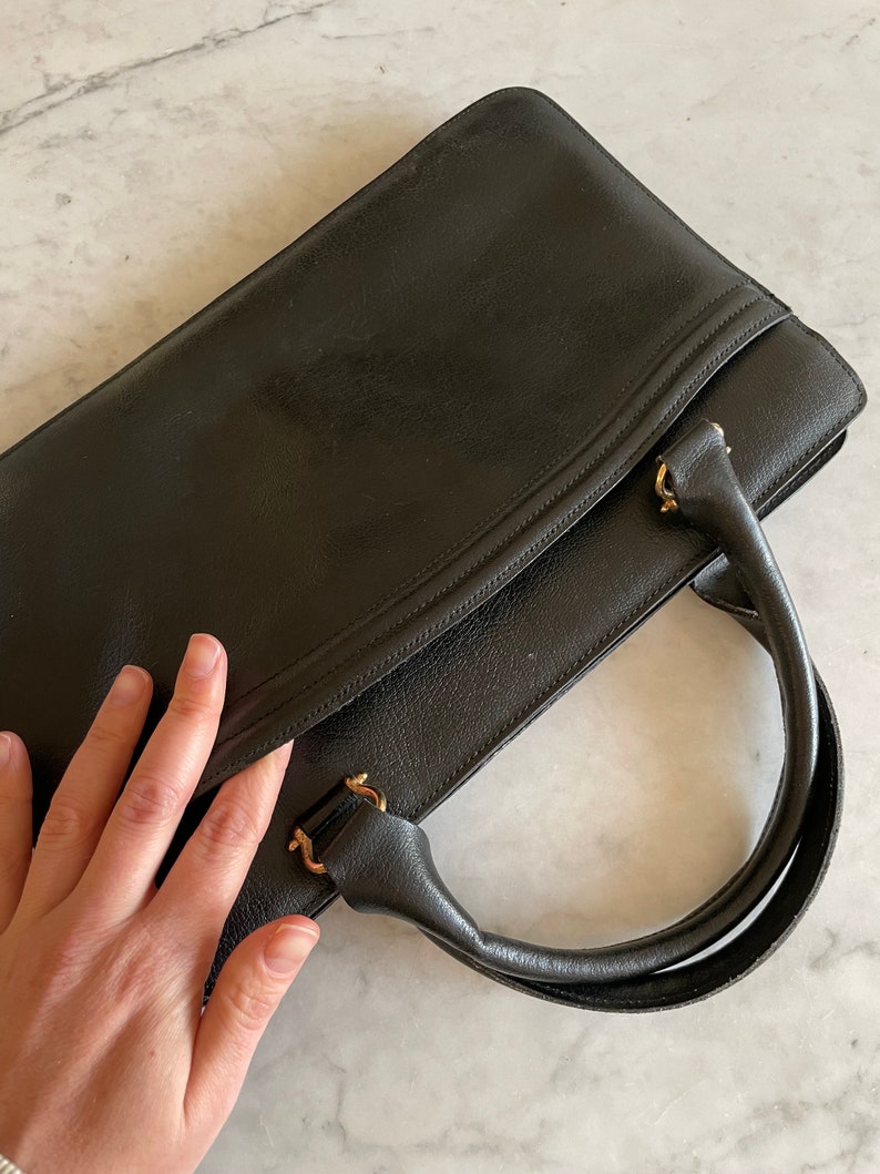 May include: A black leather briefcase with gold hardware and a single top handle.