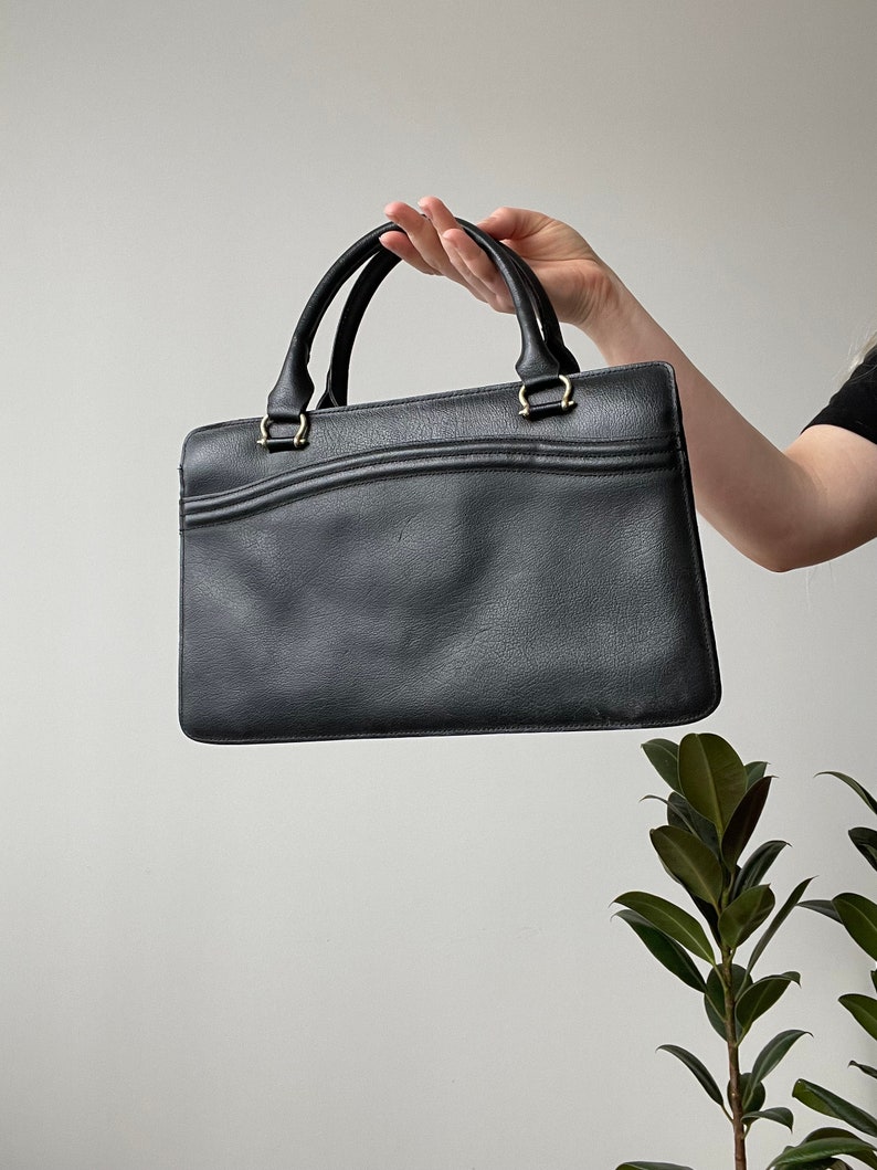 May include: A black leather handbag with two top handles and a gold clasp.