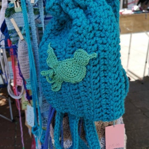 May include: A teal blue crocheted drawstring bag with a green crocheted bird applique. The bag has a price tag that reads "$15.00".