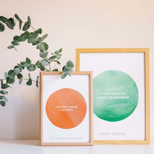 Può includere: Due stampe incorniciate con cerchi ad acquerello e affermazioni. La stampa a sinistra è arancione e dice "Non inseguo, attraggo" e "Chakra del plesso solare". La stampa a destra è verde e dice "Amo la ricchezza, amo l'abbondanza" e "Chakra del cuore".