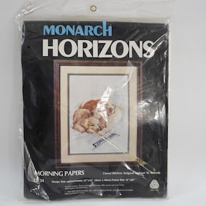 May include: Monarch Horizons cross stitch pattern, Morning Papers, featuring two dogs sleeping on a newspaper. The design size is approximately 12" x 15" (30cm x 38cm) and the frame size is 16" x 20" (41cm x 51cm).