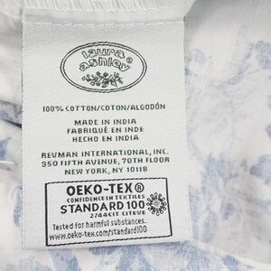 May include: A white fabric tag with the "Laura Ashley" logo, text indicating 100% cotton, and "Made in India." The tag also includes the OEKO-TEX Standard 100 certification and the address of Revman International in New York.