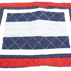 Puede incluir: Almohada acolchada rectangular con borde rojo, centro blanco y secciones estampadas en azul y blanco. Las secciones azules presentan un patrón de puntada de diamante, y las secciones blancas tienen un pequeño patrón de cuadros. La almohada es probablemente para la decoración del hogar.